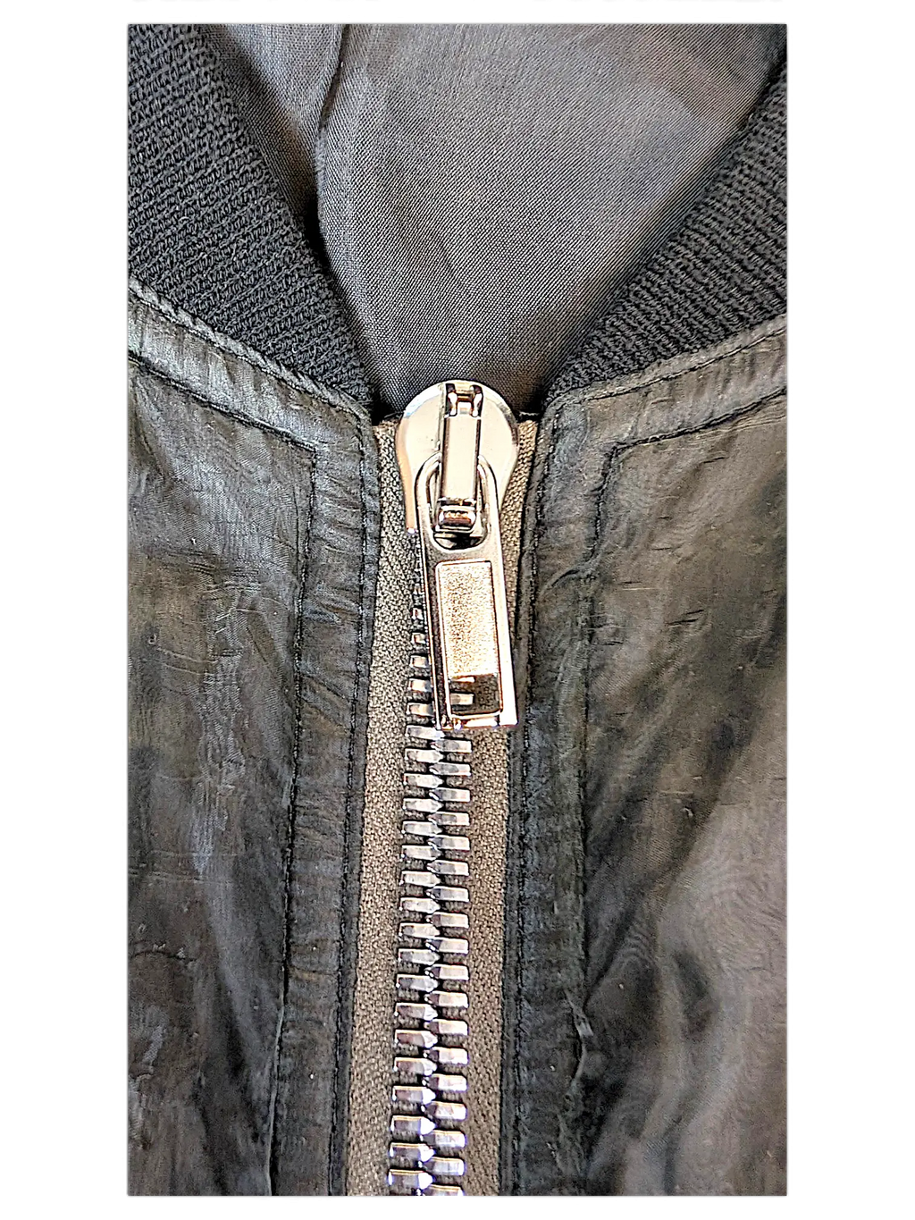 Close-up of a black JAKE & IPI Rick Owens bomber jacket featuring a metallic silver zipper and ribbed collar.
