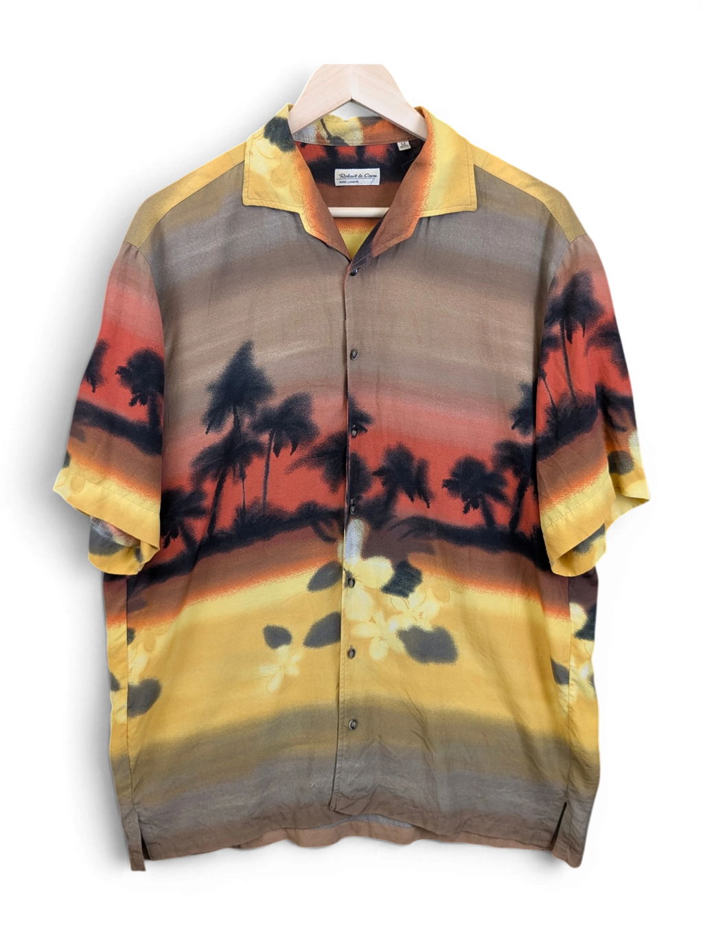 JAKE & IPI Robert Le Cam Hawaiian shirt featuring a sunset tropical palm tree print in warm yellow, orange, and brown.