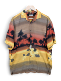 JAKE & IPI Robert Le Cam Hawaiian shirt featuring a sunset tropical palm tree print in warm yellow, orange, and brown.