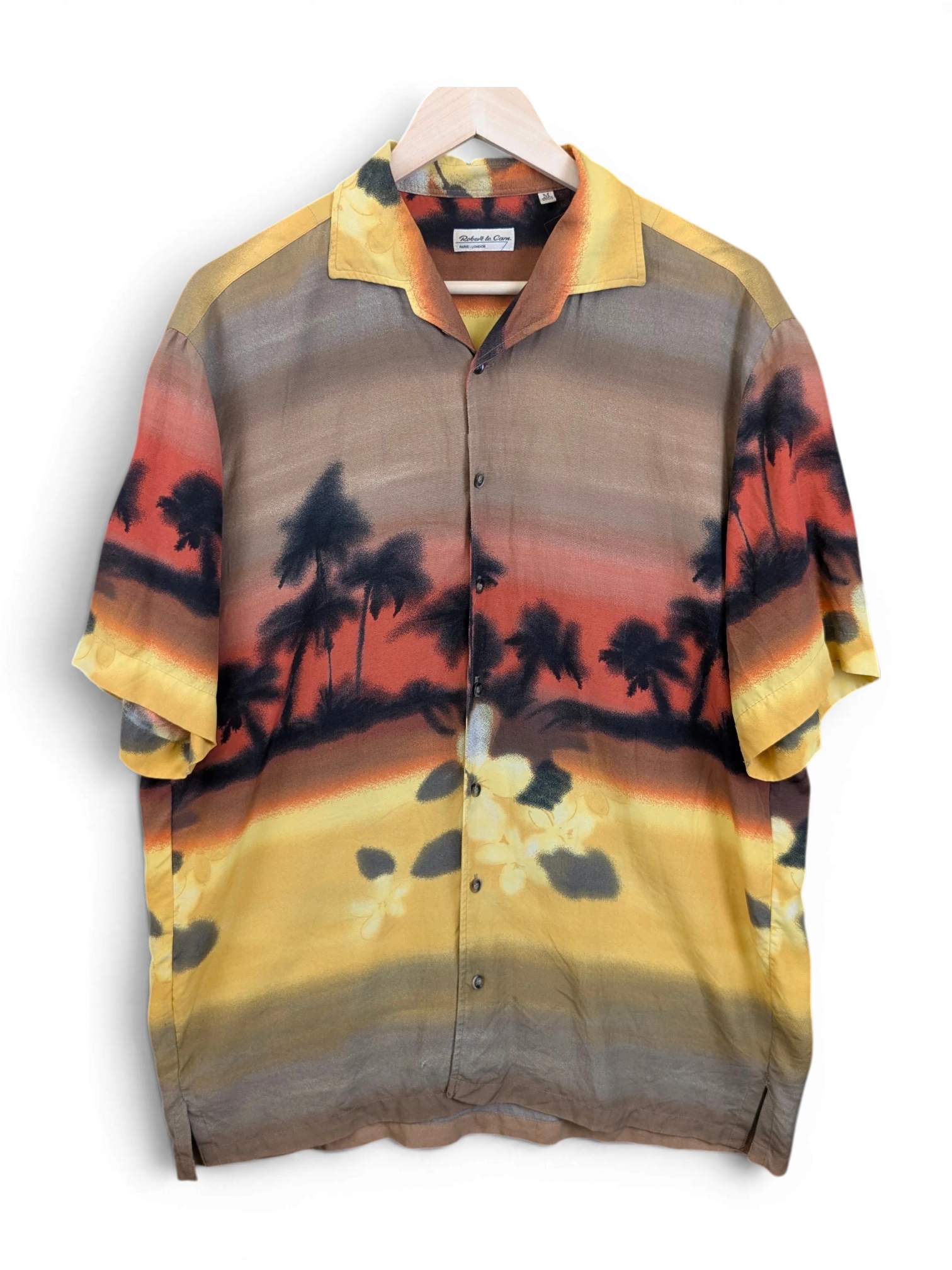 JAKE & IPI Robert Le Cam Hawaiian shirt featuring a sunset tropical palm tree print in warm yellow, orange, and brown.