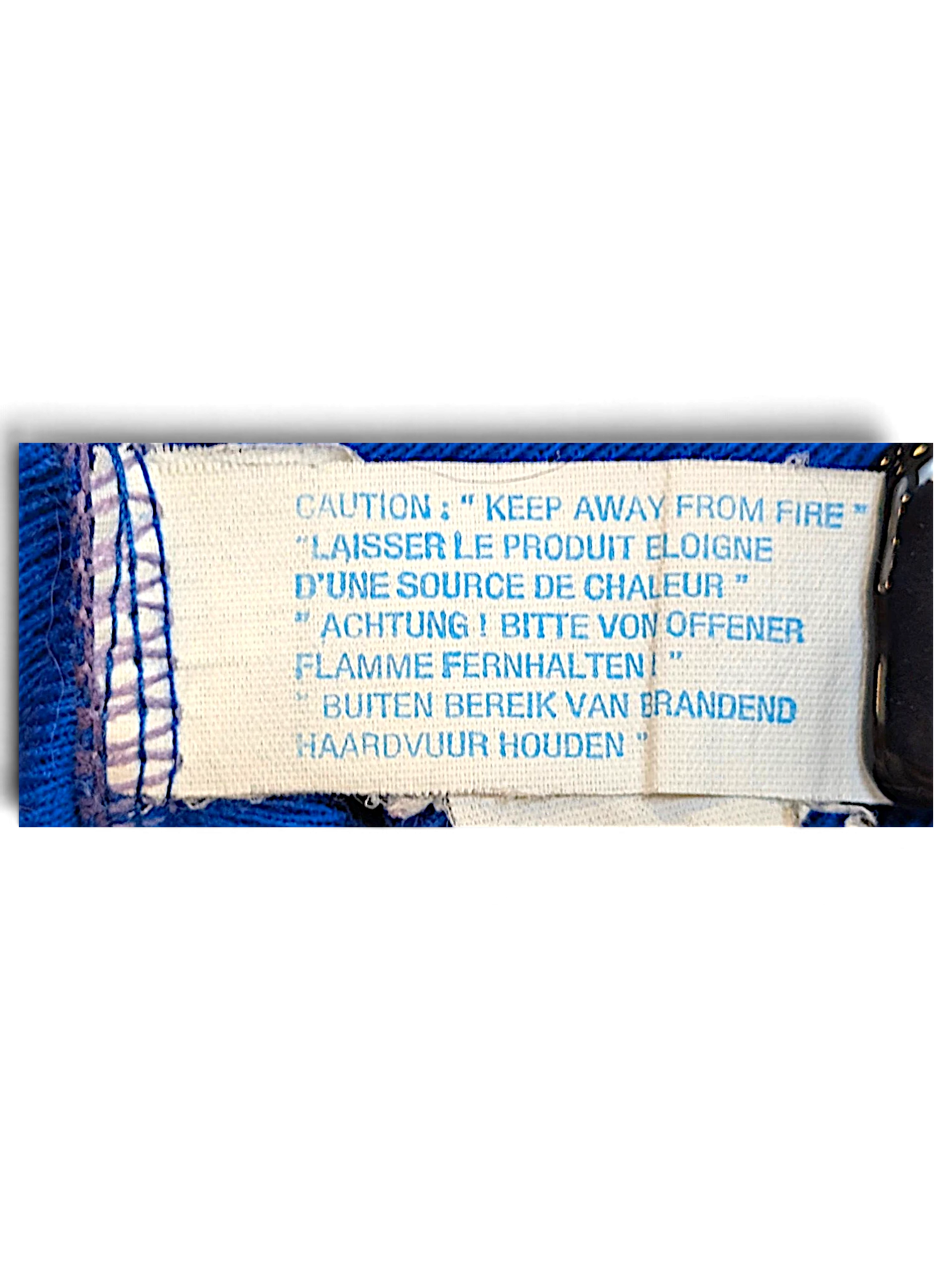 JAKE & IPI Rucanor track pants care label with multilingual fire safety warning text on a royal blue fabric background
