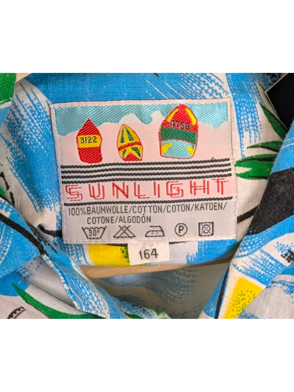 JAKE & IPI vintage Sunlight Hawaiian shirt label featuring colorful surfboard graphics on blue cotton fabric