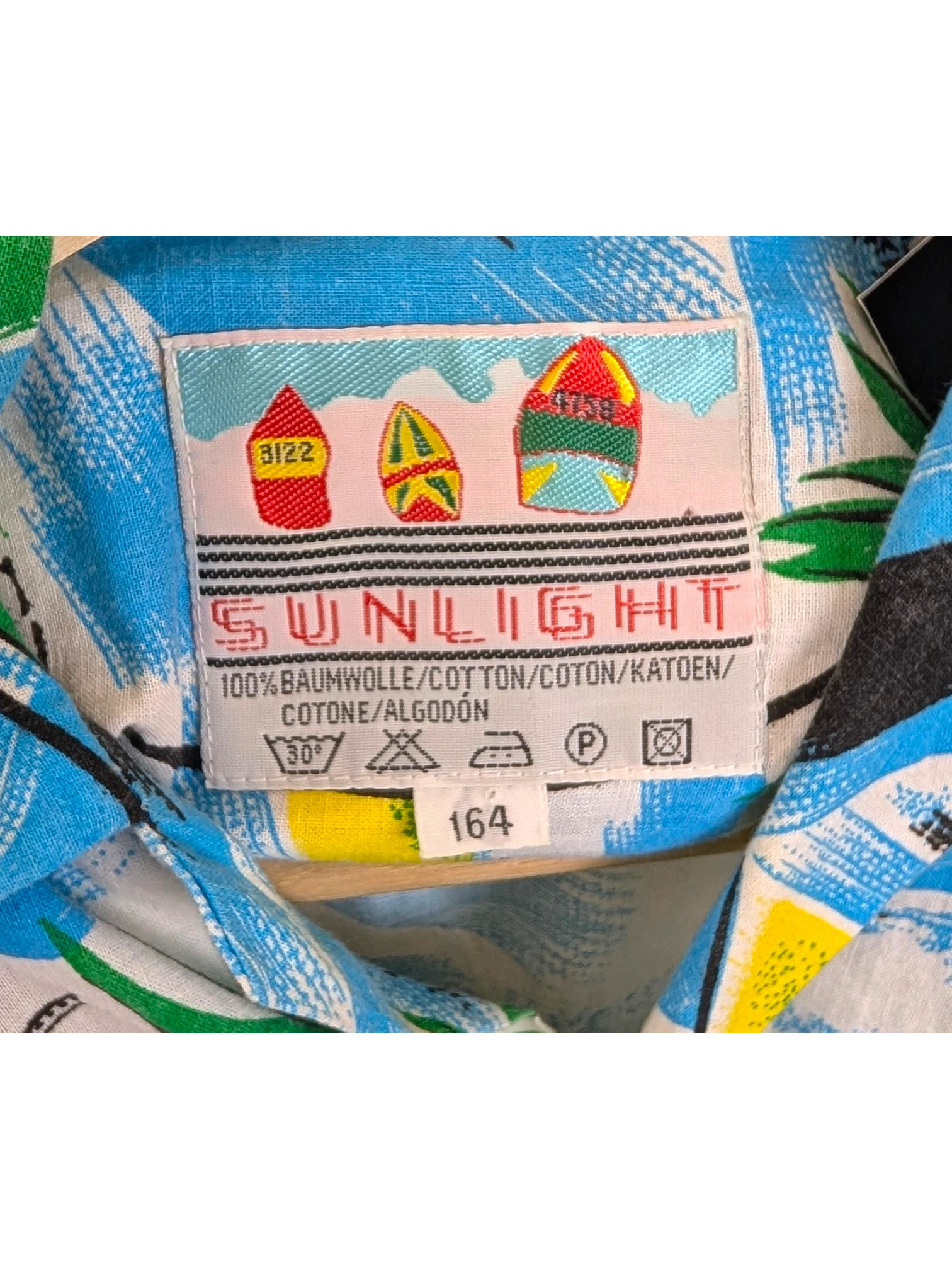 JAKE & IPI vintage Sunlight Hawaiian shirt label featuring colorful surfboard graphics on blue cotton fabric