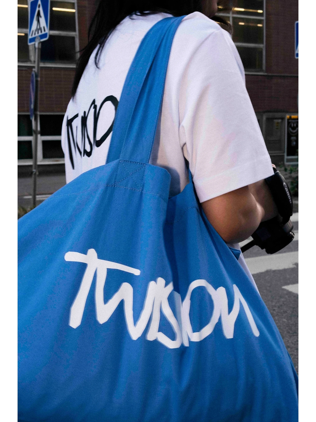 JAKE & IPI Twision blue canvas tote bag with white logo lettering carried over the shoulder by a person
