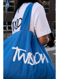 JAKE & IPI Twision blue canvas tote bag with white logo lettering carried over the shoulder by a person