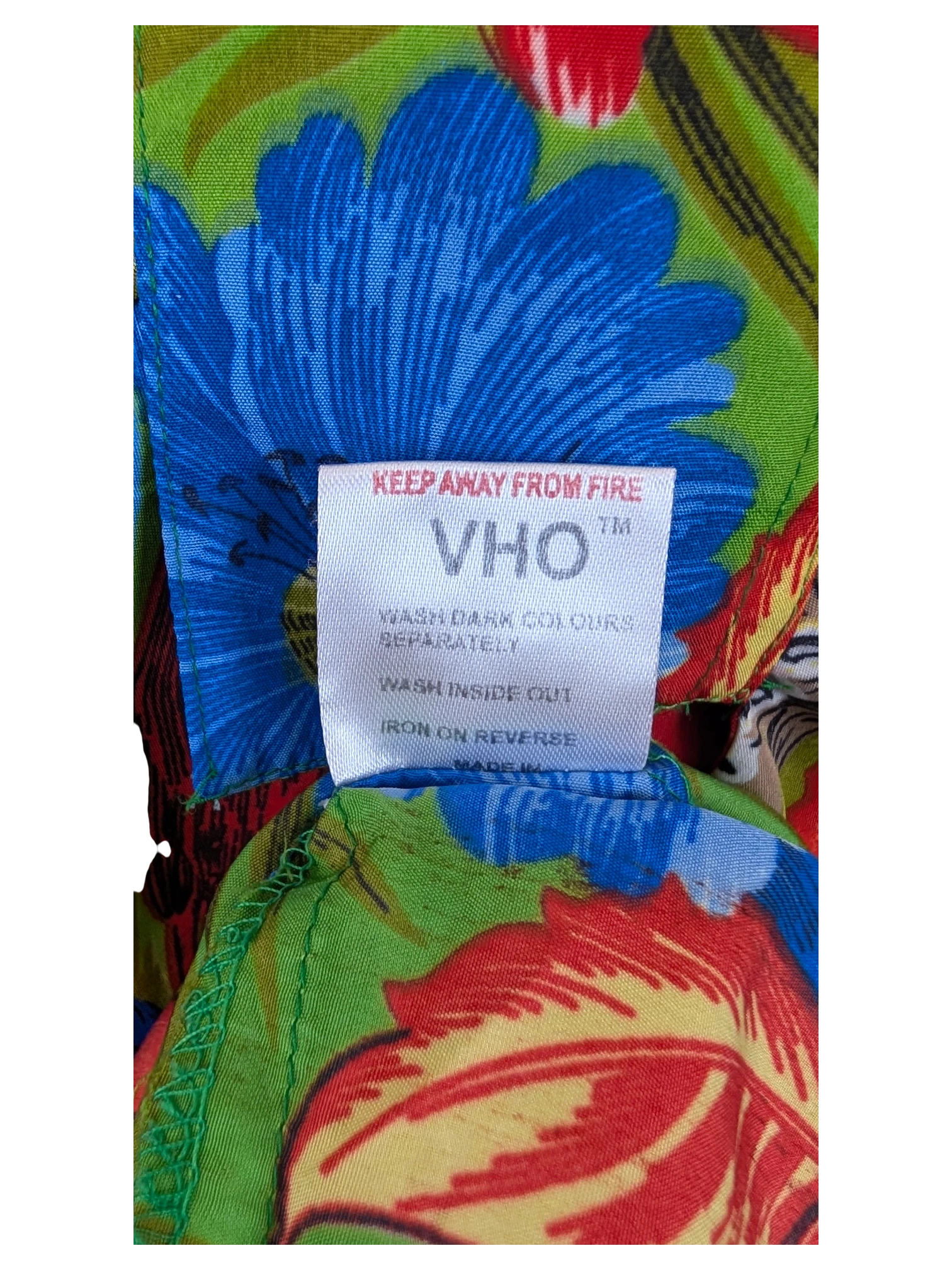 JAKE & IPI V.H.O Hawaiian shirt label with care instructions on a vibrant floral pattern background