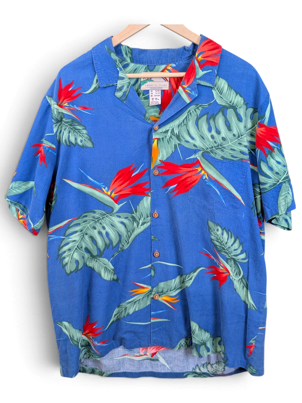 JAKE & IPI vintage blue Hawaiian shirt with red bird of paradise flowers and green tropical leaves on a wooden hanger