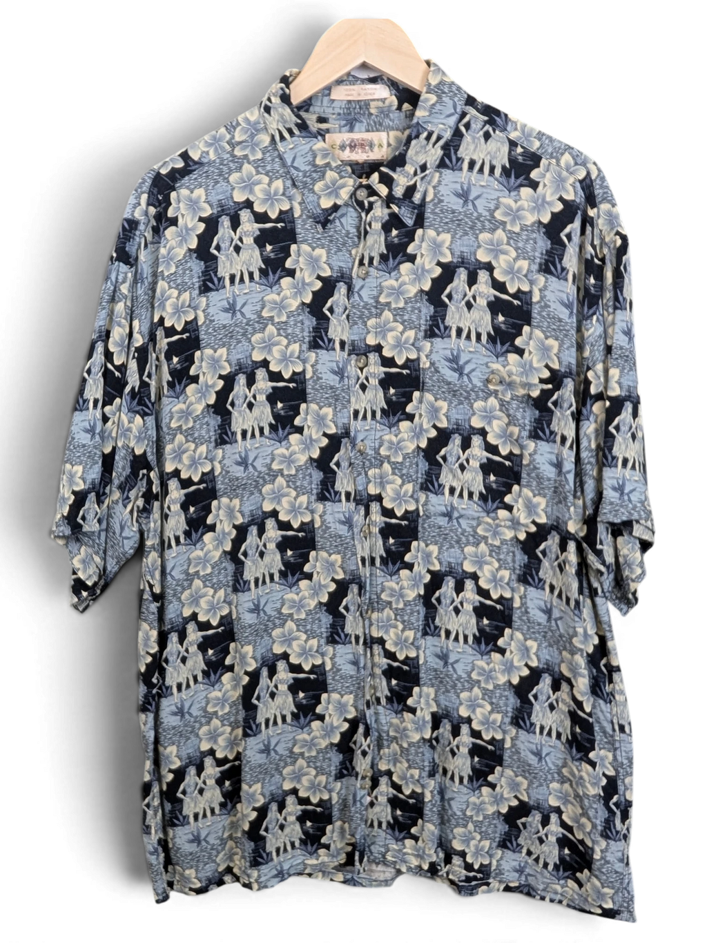 JAKE & IPI vintage 90s Campia Hawaiian shirt in blue with hula dancer and hibiscus floral print on a wooden hanger