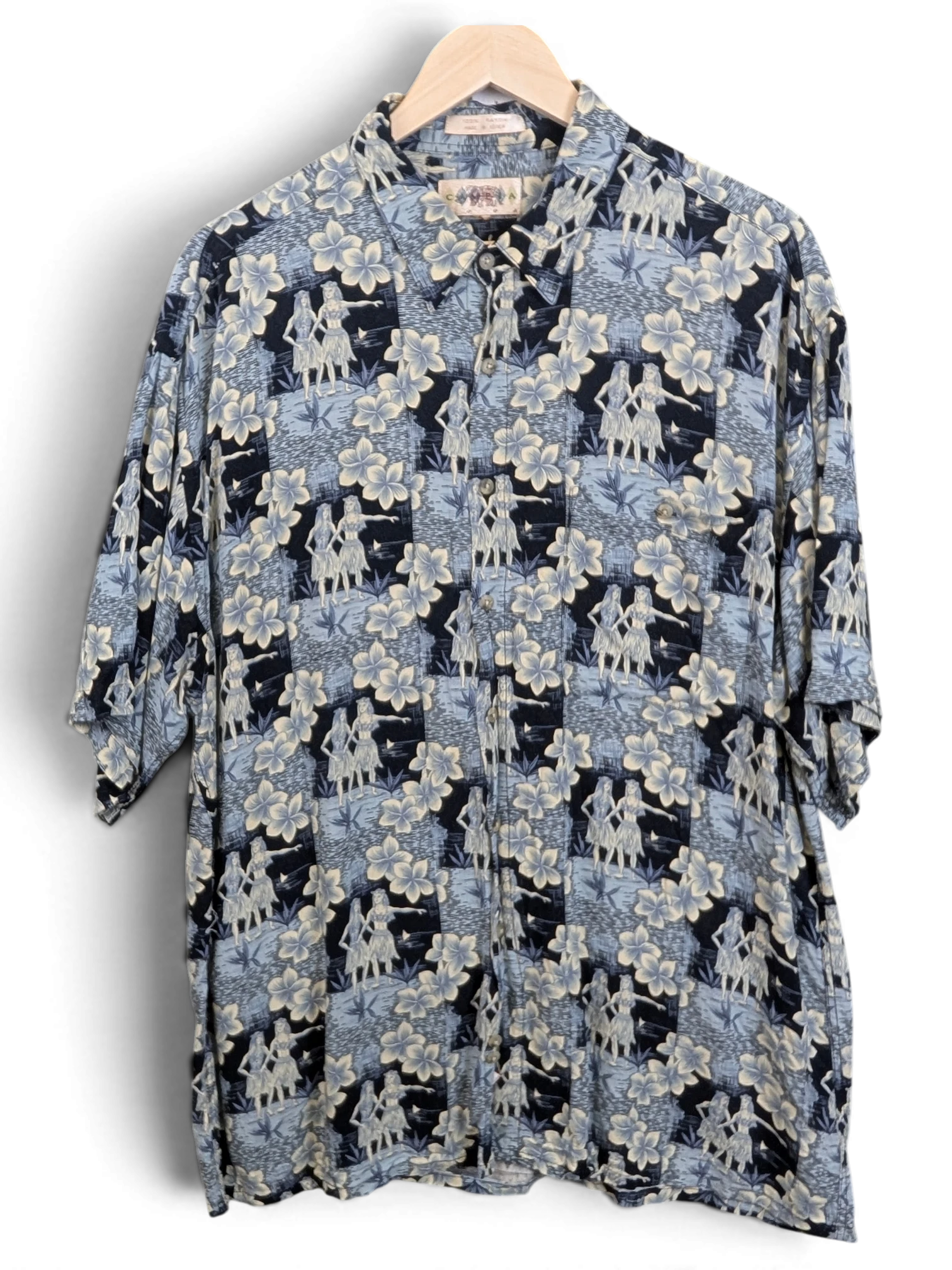JAKE & IPI vintage 90s Campia Hawaiian shirt in blue with hula dancer and hibiscus floral print on a wooden hanger